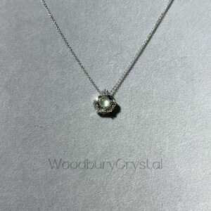 Puede incluir: Un collar de plata con un colgante en forma de coraz&oacute;n que presenta una piedra preciosa verde claro rodeada de piedras preciosas transparentes m&aacute;s peque&ntilde;as. El colgante est&aacute; engastado en un dise&ntilde;o de corona.