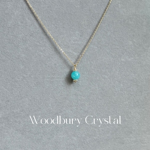 May include: A delicate gold chain necklace with a single turquoise gemstone pendant.