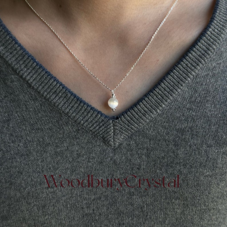 May include: A silver chain necklace with a white gemstone pendant. The pendant is round and has a slight shimmer.
