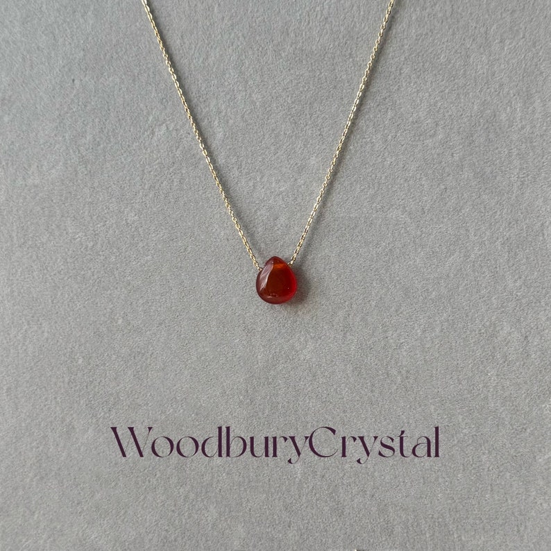 Peut inclure: Un collier d&eacute;licat en cha&icirc;ne dor&eacute;e avec un pendentif en forme de larme en cornaline. Le pendentif est de couleur rouge fonc&eacute;.