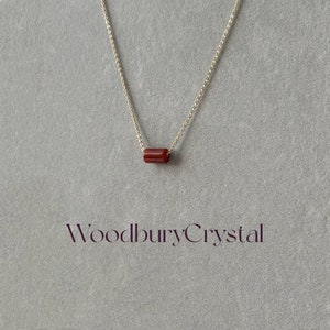 May include: A gold chain necklace with a single, red, rectangular gemstone pendant. The pendant is a simple, minimalist design. The text "WoodburyCrystal" is visible at the bottom of the image.