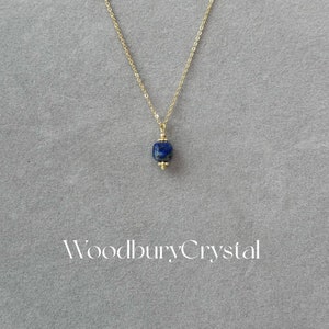 Peut inclure: Un collier en cha&icirc;ne dor&eacute;e avec un pendentif en lapis-lazuli bleu fonc&eacute;. Le pendentif est de forme carr&eacute;e aux bords arrondis. Le collier est sur un fond gris avec le texte "Woodbury Crystal" imprim&eacute; sous le collier.