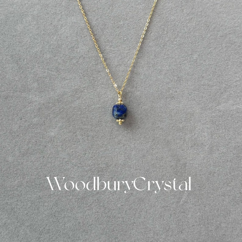 Peut inclure: Un collier en cha&icirc;ne dor&eacute;e avec un pendentif en lapis-lazuli bleu fonc&eacute;. Le pendentif est de forme carr&eacute;e aux bords arrondis. Le collier est sur un fond gris avec le texte "Woodbury Crystal" imprim&eacute; sous le collier.