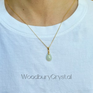 Puede incluir: Un delicado collar de cadena de oro con un colgante de jade verde claro en forma de l&aacute;grima. El colgante tiene una anilla de oro y est&aacute; colocado sobre un fondo blanco.