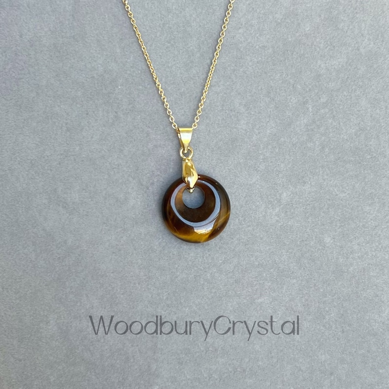 May include: Gold chain necklace with a round tiger's eye pendant. The pendant has a gold setting and a hole in the center.