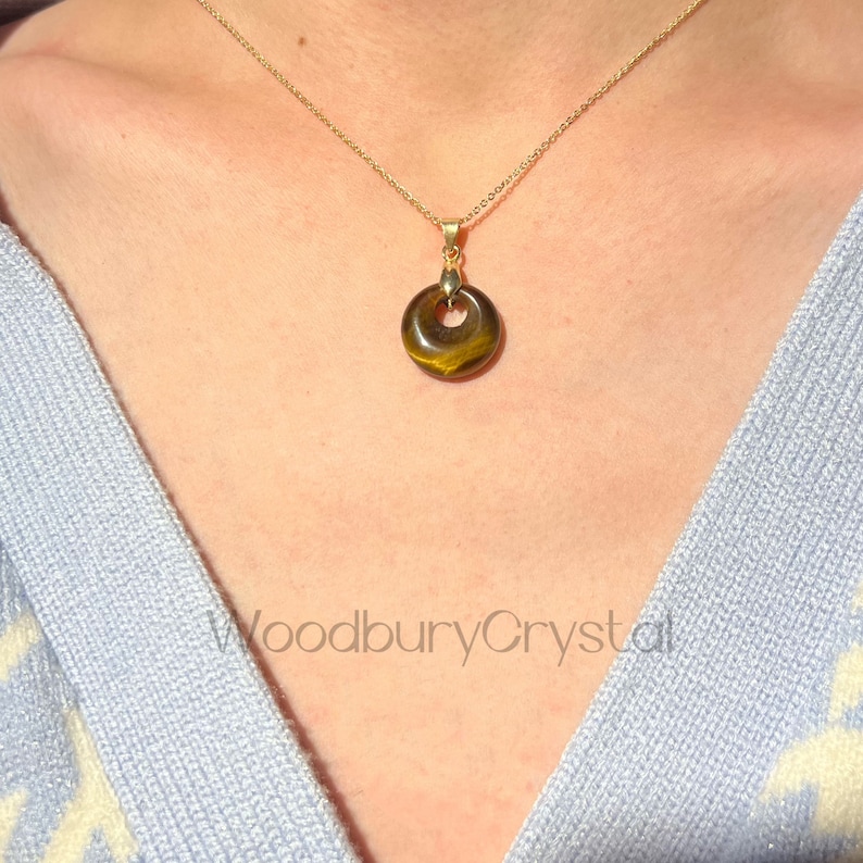 May include: A gold chain necklace with a round tiger's eye pendant. The pendant has a hole in the center and is a light brown color with gold flecks.
