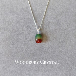 May include: A silver chain necklace with a green, red, and brown agate pendant. The pendant is oval shaped and has a smooth, polished finish. The necklace is on a gray background with the text "WOODBURY CRYSTAL" below the pendant.