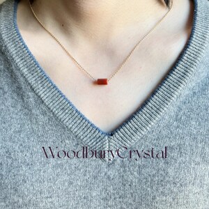 May include: A gold chain necklace with a single, rectangular, red carnelian gemstone pendant.