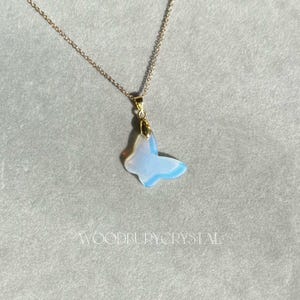 May include: A delicate gold chain necklace with a iridescent blue butterfly pendant. The butterfly is made of opal and has a gold-toned finish.
