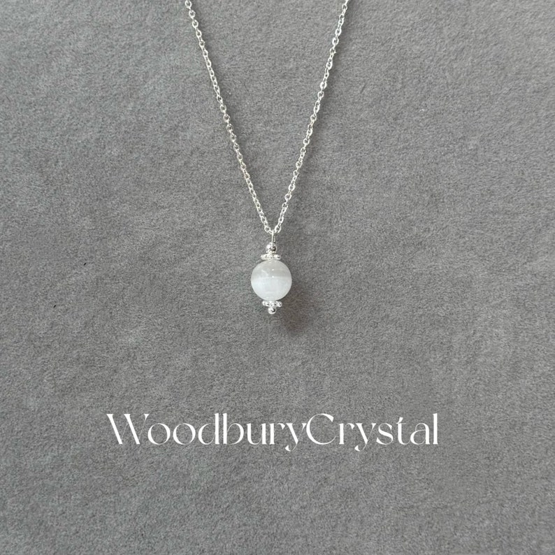 May include: A silver chain necklace with a white gemstone pendant. The pendant is a round, faceted bead with a silver bail.
