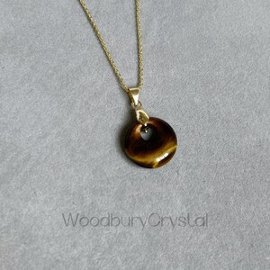 May include: A gold chain necklace with a round tiger's eye pendant. The pendant has a hole in the center in the shape of a heart.