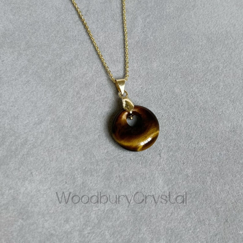 May include: A gold chain necklace with a round tiger's eye pendant. The pendant has a hole in the center in the shape of a heart.