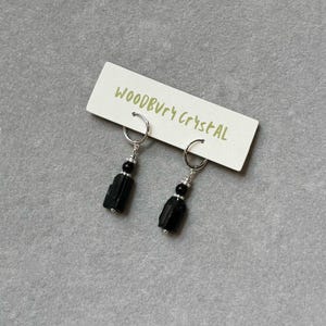 May include: A pair of black tourmaline earrings with silver hoops and black beads. The earrings are displayed on a white card with the text "Woodbury Crystal".