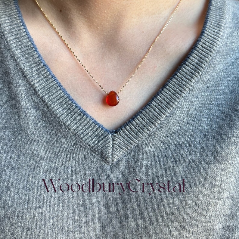 Peut inclure: Un collier en cha&icirc;ne dor&eacute;e avec un pendentif en forme de larme en cornaline. Le collier est port&eacute; par une personne avec un pull gris.