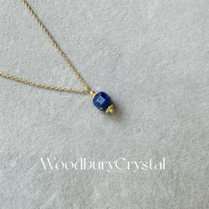 Peut inclure: Un collier en cha&icirc;ne dor&eacute;e avec un pendentif en pierre pr&eacute;cieuse bleu fonc&eacute;. Le pendentif est facett&eacute; et comporte une perle dor&eacute;e en haut.