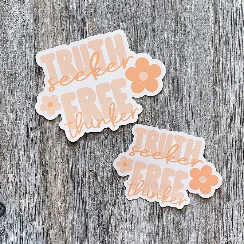 Op de afbeelding: Twee stickers met de woorden "TRUTH seeker FREE thinker" in een retro lettertype, met perzik kleurige bloemen. De stickers hebben een witte achtergrond en een perzik- en lichtoranje kleurenschema. De stickers liggen op een houten oppervlak.