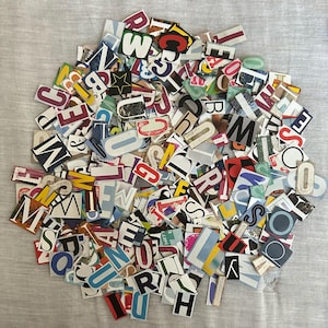 May include: A collection of colorful paper cut-out letters and numbers in various fonts and sizes. The letters are arranged in a circular shape, with a mix of colors including red, blue, yellow, and green. The background is a light gray fabric.