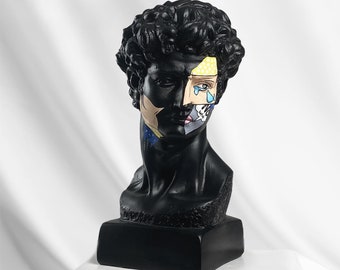 May include: Black and white bust sculpture of a man with a pop art design on his face. The design features a yellow, blue, and white pattern with a tear drop and a hand.