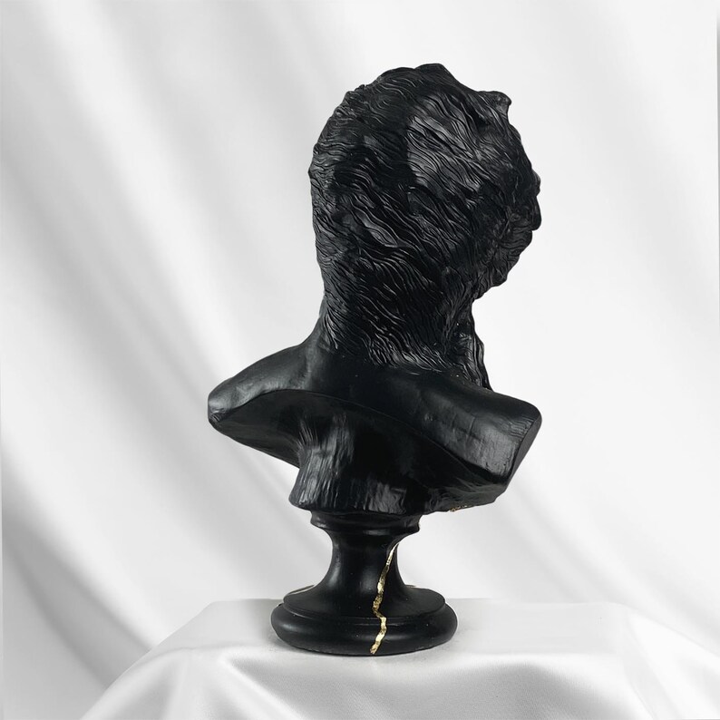 Puede incluir: Busto de escultura en negro y dorado de la cabeza y los hombros de una persona. El busto est&aacute; sobre un pedestal negro con detalles dorados.