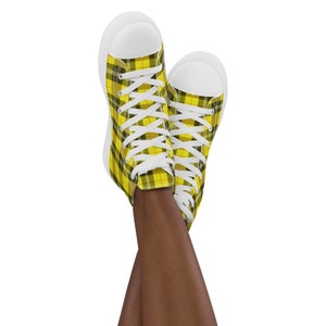 May include: A pair of high-top canvas shoes with yellow and black plaid pattern. The shoes are white with white laces.