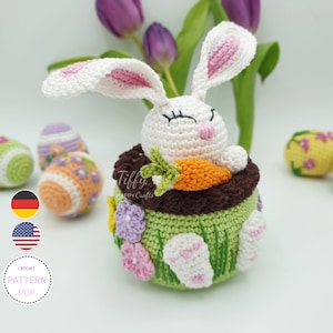 May include: Crochet pattern for a white bunny holding a carrot, sitting in a green pot with flowers and grass. The pot is brown on the inside and has white bunny footprints on the outside. The pattern is available in PDF format.