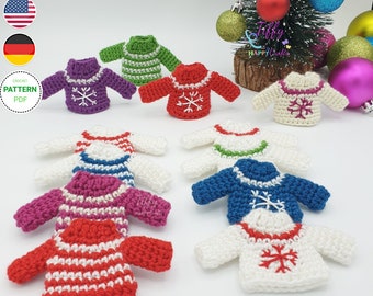 May include: A collection of nine miniature crocheted sweaters in various colors, including red, white, blue, green, purple, and pink. Each sweater features a snowflake design and a white trim around the neck and cuffs. The sweaters are arranged on a white surface.