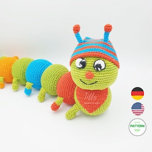 Könnte beinhalten: Ein gehäkeltes Raupenspielzeug mit einem grünen Körper, orangefarbenen und blauen Segmenten und einer rot-blau gestreiften Mütze. Die Raupe hat ein lächelndes Gesicht mit schwarzen Augen und einer roten Nase. Das Spielzeug befindet sich auf einem weißen Hintergrund.