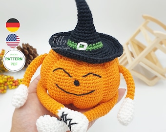 Puede incluir: Una calabaza de crochet con un sombrero de bruja negro con una banda verde. La calabaza tiene una cara sonriente y brazos y piernas de crochet naranja y blanco.