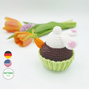 Peut inclure: Patron de crochet pour un amigurumi cupcake lapin. Le cupcake est brun avec un glaçage vert et une tête de lapin blanche avec des oreilles roses. Le lapin tient une carotte.