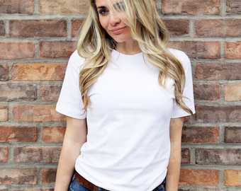 May include: A woman wearing a white t-shirt with a brick wall background.