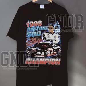 Peut inclure: Un t-shirt noir &agrave; manches courtes avec une impression graphique du Daytona 500 de 1998. Le motif comprend un portrait de Dale Earnhardt Jr., une voiture de course noire num&eacute;ro 3, un drapeau &agrave; damier et le texte 1998 DAYTONA 500 et CHAMPION.