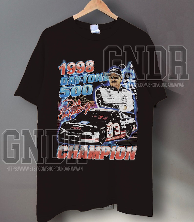 Peut inclure: Un t-shirt noir &agrave; manches courtes avec une impression graphique du Daytona 500 de 1998. Le motif comprend un portrait de Dale Earnhardt Jr., une voiture de course noire num&eacute;ro 3, un drapeau &agrave; damier et le texte 1998 DAYTONA 500 et CHAMPION.