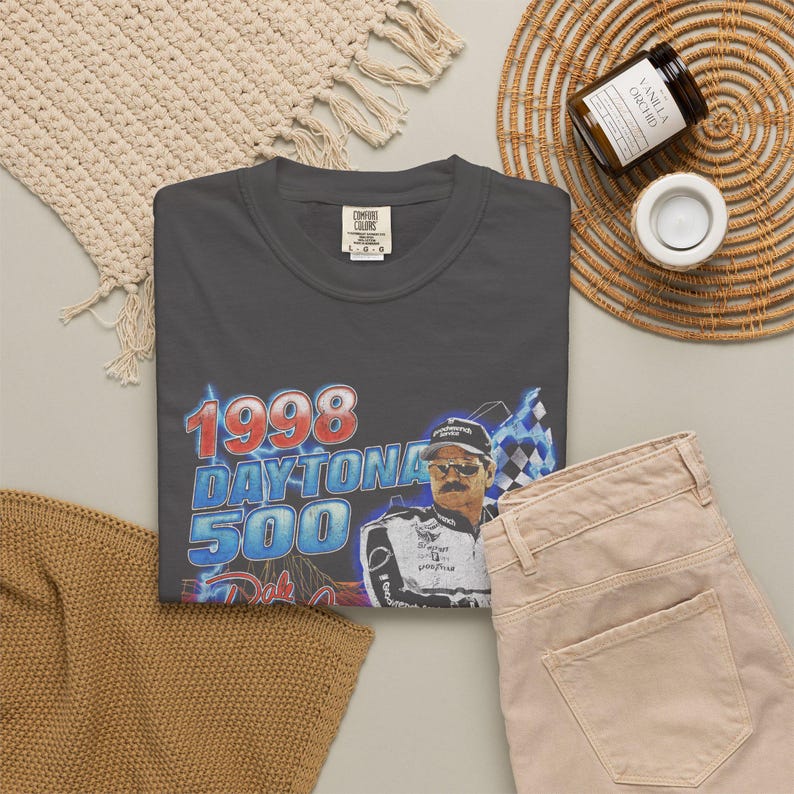 Peut inclure: Un t-shirt &agrave; col rond gris anthracite avec une impression graphique du Daytona 500 de 1998, repr&eacute;sentant un pilote de course portant des lunettes de soleil et une combinaison, avec des &eacute;clairs bleus et un motif de drapeau &agrave; damier.