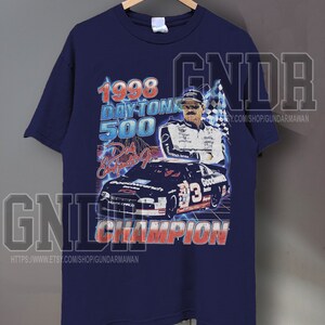 Peut inclure: Un t-shirt bleu marine &agrave; manches courtes avec une impression graphique du Daytona 500 de 1998. Le motif comprend une voiture de course, un pilote, un drapeau &agrave; damier et le texte 1998 DAYTONA 500, Dale Earnhardt Jr. et CHAMPION en rouge et blanc.