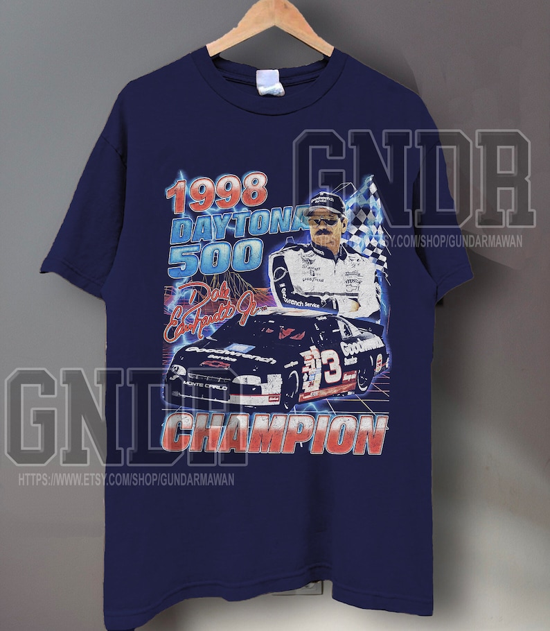 Peut inclure: Un t-shirt bleu marine &agrave; manches courtes avec une impression graphique du Daytona 500 de 1998. Le motif comprend une voiture de course, un pilote, un drapeau &agrave; damier et le texte 1998 DAYTONA 500, Dale Earnhardt Jr. et CHAMPION en rouge et blanc.
