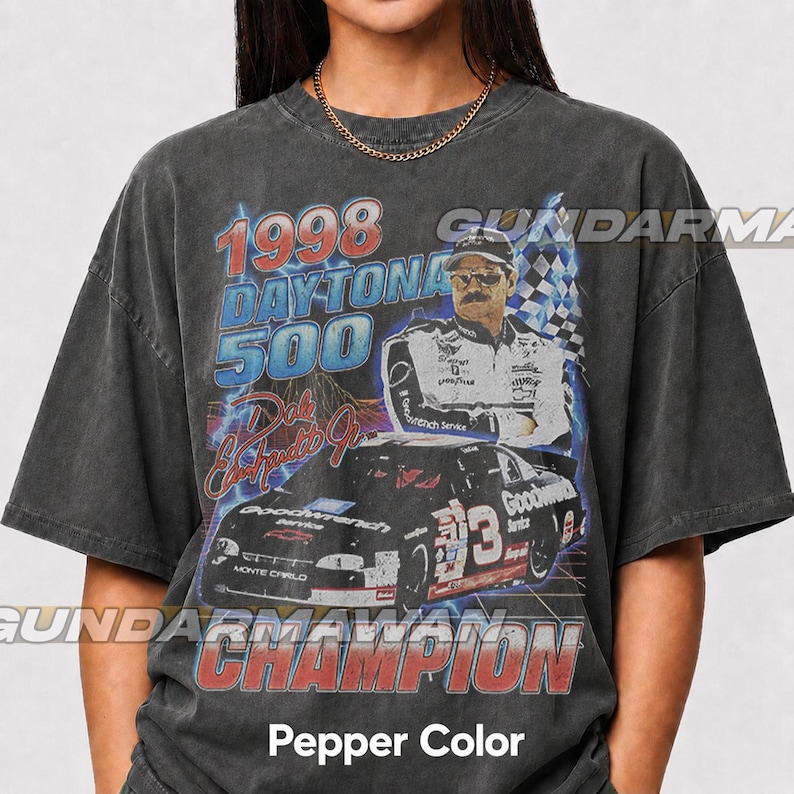Peut inclure: Un t-shirt gris anthracite &agrave; manches courtes avec une impression graphique du Daytona 500 de 1998, un portrait de Dale Earnhardt Jr. et sa voiture de course num&eacute;ro 3. Le design inclut le texte 1998 Daytona 500, Dale Earnhardt Jr. et Champion.