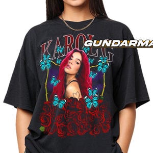 May include: Black t-shirt featuring a graphic of a woman with red hair, surrounded by blue butterflies and red roses. The word "KAROL" is printed above the graphic in a stylized font. The shirt has a vintage, worn look.