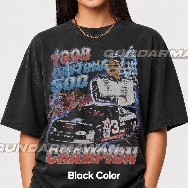 Peut inclure: Un t-shirt noir avec une impression graphique du Daytona 500 de 1998, Dale Earnhardt Jr. et sa voiture de course num&eacute;ro 3. Le design comprend des &eacute;clairs bleus, un drapeau &agrave; damier et le texte 1998 DAYTONA 500 et CHAMPION en rouge et bleu.