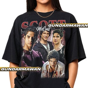 Pode incluir: Camiseta preta com um gráfico de Scott McCall da série de TV Teen Wolf. O design inclui várias imagens do personagem com o nome "Scott McCall" em fonte vermelha e branca. Gráficos de raios também estão presentes.