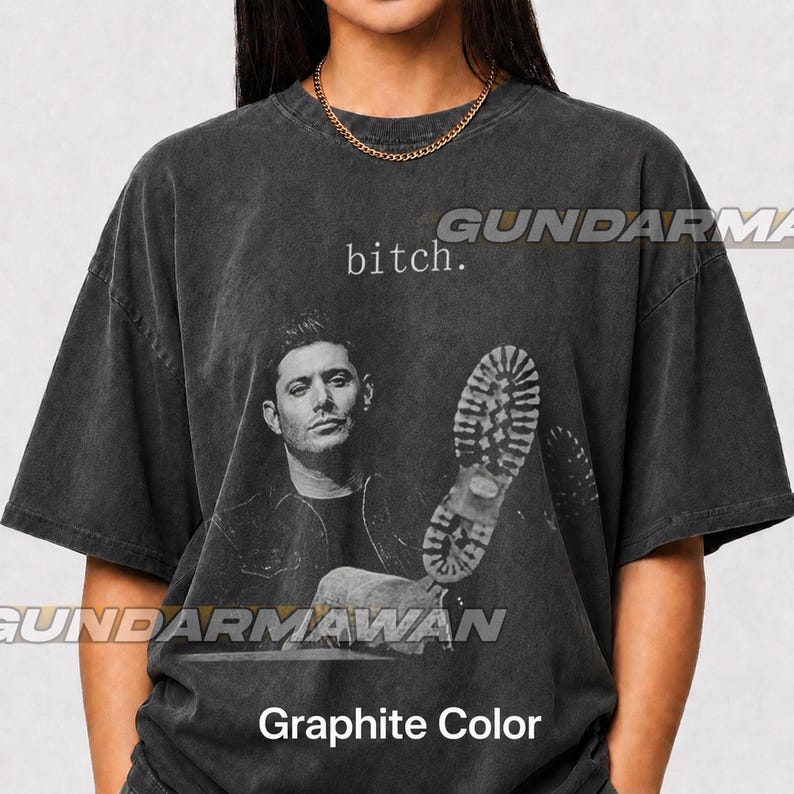 May include: A graphite-colored, short-sleeved t-shirt featuring a black and white photographic print of a man and a large boot sole graphic. The text "bitch." is printed in a small, serif font above the man's head. The shirt has a crew neckline.