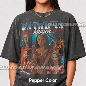 May include: A charcoal gray t-shirt featuring a graphic print of a person in various poses and expressions. The text PATRICIA Moyer is printed in a bold, stylized font at the top. The design includes blue and red accents with lightning effects.