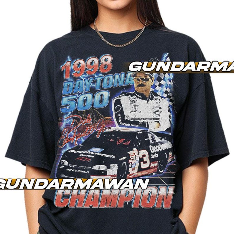 Peut inclure: Un t-shirt noir &agrave; manches courtes avec une impression graphique du Daytona 500 de 1998. Le motif comprend un portrait de Dale Earnhardt, une voiture de course noire num&eacute;ro 3, et le texte 1998 DAYTONA 500, Dale Earnhardt Jr, et CHAMPION.
