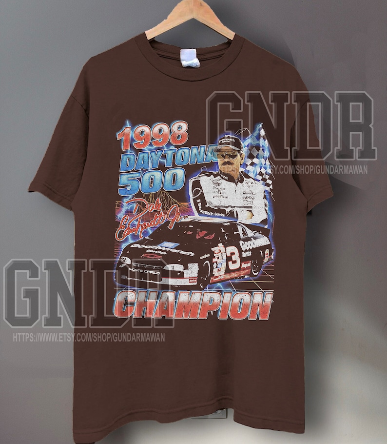 Peut inclure: Un t-shirt marron &agrave; manches courtes avec une impression graphique du Daytona 500 de 1998, Dale Earnhardt Jr. et une voiture de course noire portant le num&eacute;ro 3. Le texte indique 1998 DAYTONA 500, Dale Earnhardt Jr. et CHAMPION en lettres grasses.