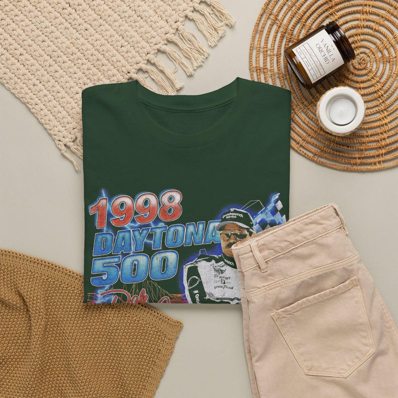 Peut inclure: Un t-shirt vert fonc&eacute; avec une impression graphique du Daytona 500 de 1998. Le motif comprend le texte 1998 DAYTONA 500 en rouge et bleu, ainsi qu'une illustration d'un pilote de course portant une casquette et des lunettes de soleil, avec un drapeau &agrave; damier.