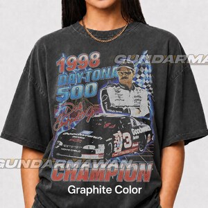 Peut inclure: Un t-shirt gris anthracite avec une impression graphique du Daytona 500 de 1998, une voiture de course portant le num&eacute;ro 3 et un portrait de Dale Earnhardt Jr. Le texte indique 1998 DAYTONA 500, Dale Earnhardt Jr. et CHAMPION. Effet d&eacute;lav&eacute;.