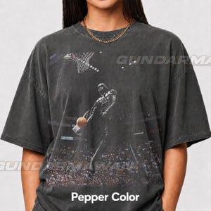 May include: A charcoal gray, vintage-wash short-sleeve t-shirt featuring a graphic print of a character resembling Darth Vader dunking a basketball in a crowded arena. The design includes a basketball hoop and the text GUNDARMA.