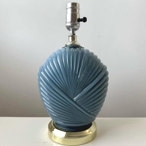 May include: A blue ceramic table lamp with a fan-shaped design. The lamp has a gold-colored base and a silver lamp holder. The lamp is approximately 12 inches tall.