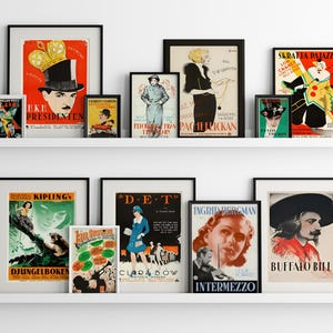 May include: A white shelf with black framed vintage movie posters. The posters feature images of actors and actresses, including Charlie Chaplin, Ingrid Bergman, and Buffalo Bill. The posters are in various colours and styles, and some have text in different languages.