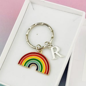 Może przedstawiać: Brelok z motywem tęczy ze srebrnym kółkiem i zawieszką z literą "R". Zawieszka w kształcie tęczy ma kolorowy wzór z czerwonym, pomarańczowym, żółtym, zielonym, niebieskim i fioletowym. Brelok jest prezentowany w białym pudełku prezentowym.