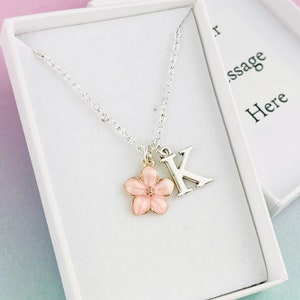 May include: A silver necklace with a pink flower charm and a silver letter K charm. The necklace is in a white gift box with the text "Your message here".